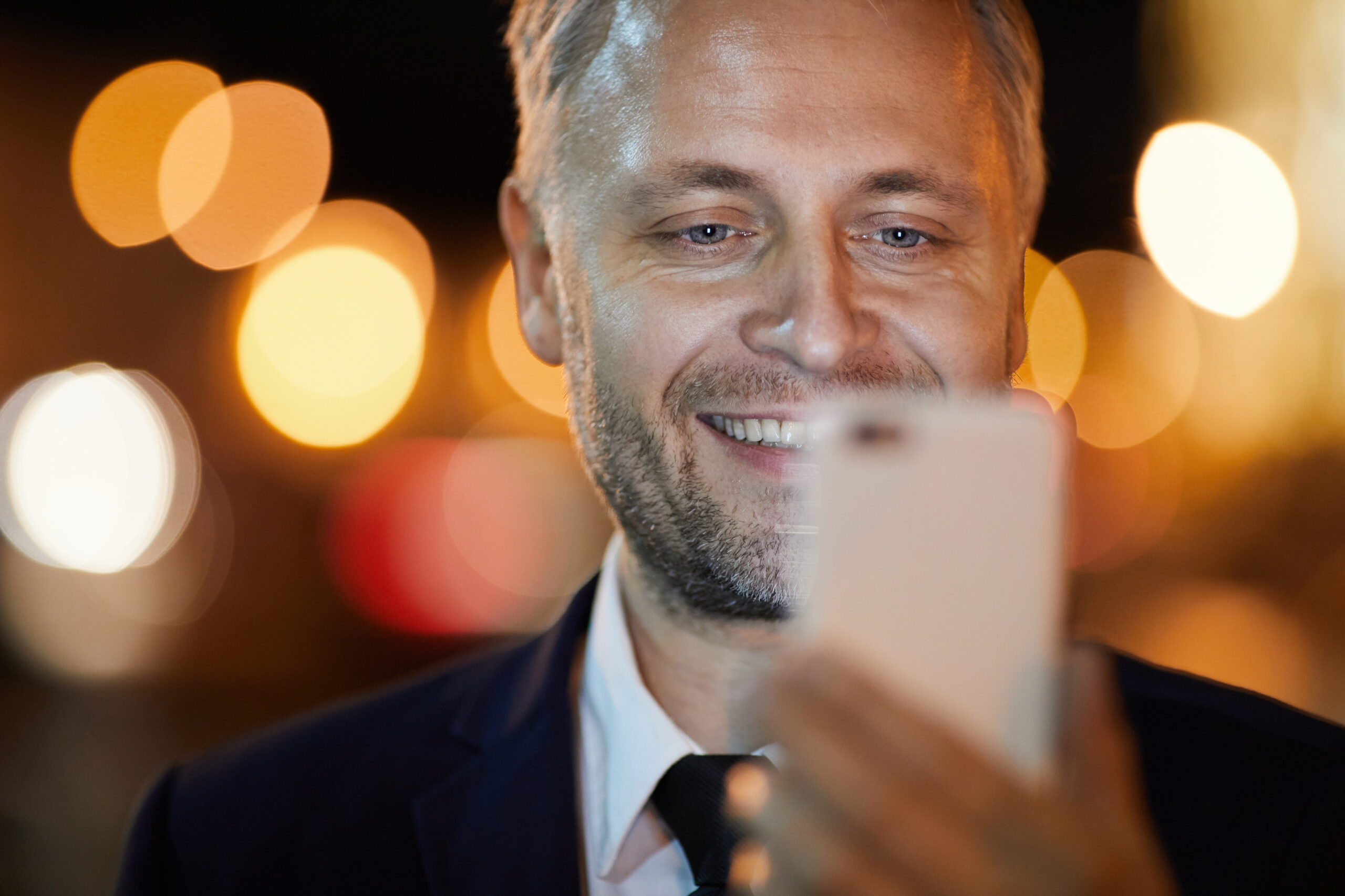 Smiling businessman looking at camera of smartphone while posing for selfie
